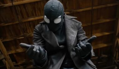 closeup of a man in black spiderman suit holding both hands out in front of him, ready to fire out webbing