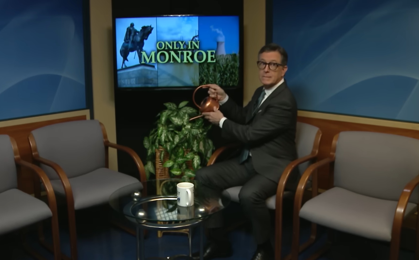 Stephen Colbert watering a plant on a television set.