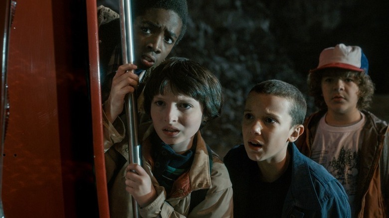 Lucas Sinclair, Mike Wheeler, Eleven, and Dustin Henderson stand shocked by a metal pole