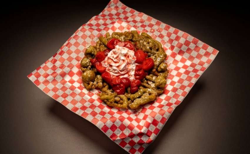 A classic crispy festival funnel cake topped with fresh strawberries and a vibrant green earthy matcha sauce drizzle.