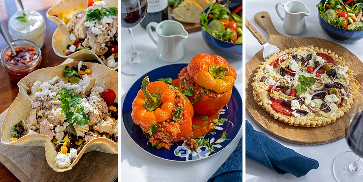 A triptych food photograph showing all three Brampton 1860 Picnic Dinner for Two entree options side by side: on the left, a Chicken Taco Salad in a crispy taco shell bowl topped with cotija cheese and cilantro with salsa on the side; in the center, three roasted stuffed orange and yellow bell peppers on a blue decorative plate with a red wine glass and green salad; and on the right, a Mediterranean Veggie Pizza on a wooden board topped with tomatoes, kalamata olives, artichoke hearts, red onion, and crumbled feta with fresh basil