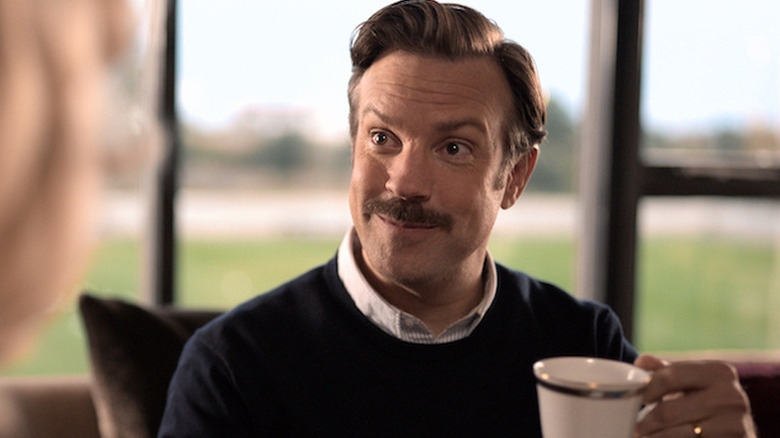 Ted Lasso smiling exuberantly while holding a teacup