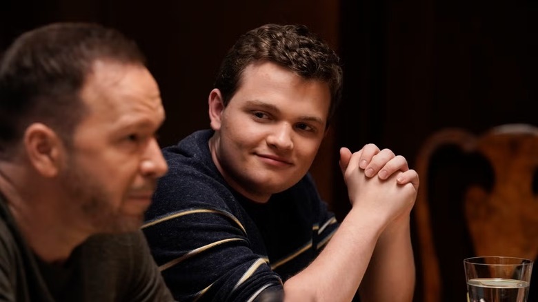 Andrew Terraciano as Sean Reagan, wearing a dark blue and white striped sweater, looking fondly at and sitting next to his father, Donnie Wahlberg as Danny Reagan, wearing a brown sweater, out of focus in the foreground in Blue Bloods