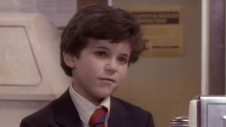 Kevin (Fred Savage) sitting at a table and wearing a suit on The Wonder Years S1E3