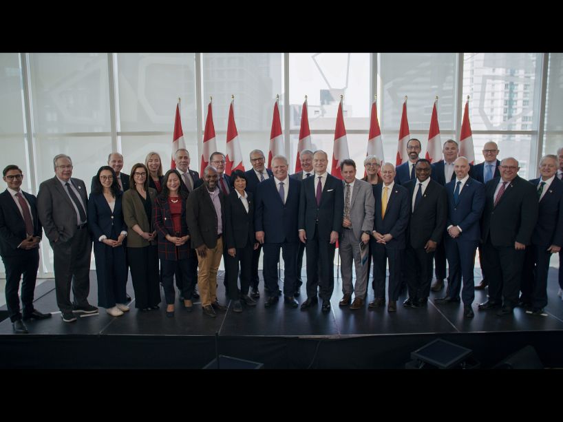 Government, business and post-secondary leaders gathered together on stage, smiling.