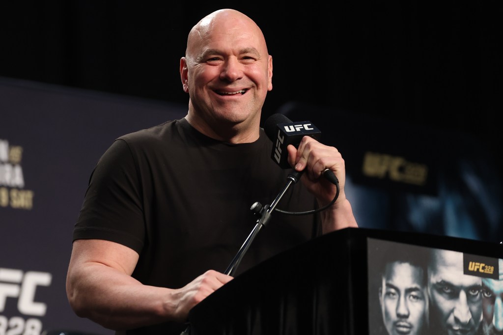 UFC President Dana White smiles while speaking into a microphone at a press conference.