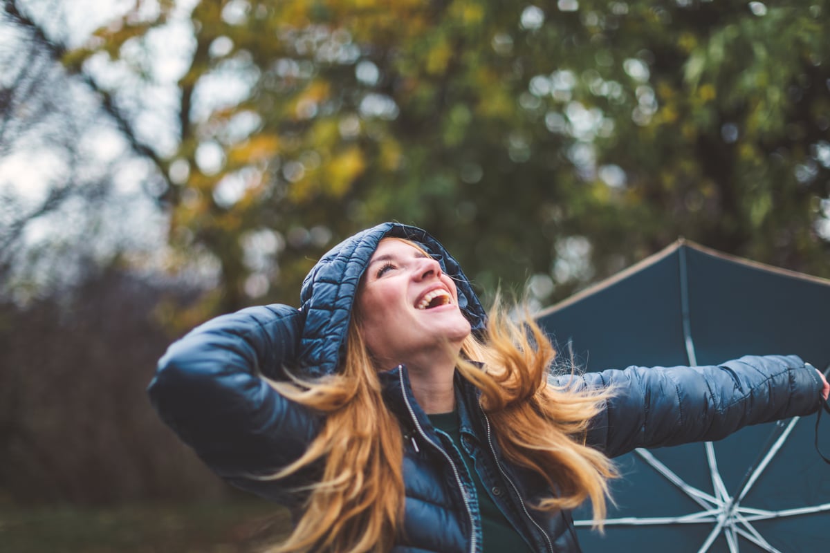 A person holding an umbrella and looking up, smiling.
