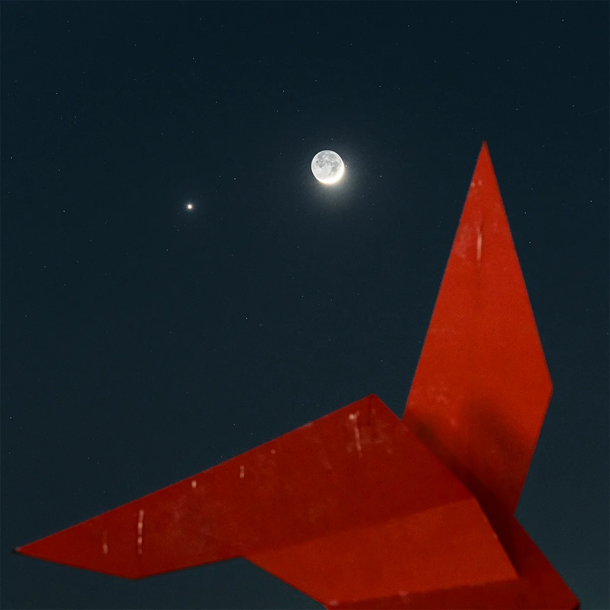 The crescent Moon and Venus framed by 'The Angel' sculpture, Ossining, New York, USA, 18 May 2026, captured by Chirag Upreti. Equipment: Sony A7R3 camera, Sony 70–200mm lens, Left tripod. Exposure: ISO 1600, f/4.5, 2.5 sec shutter speed