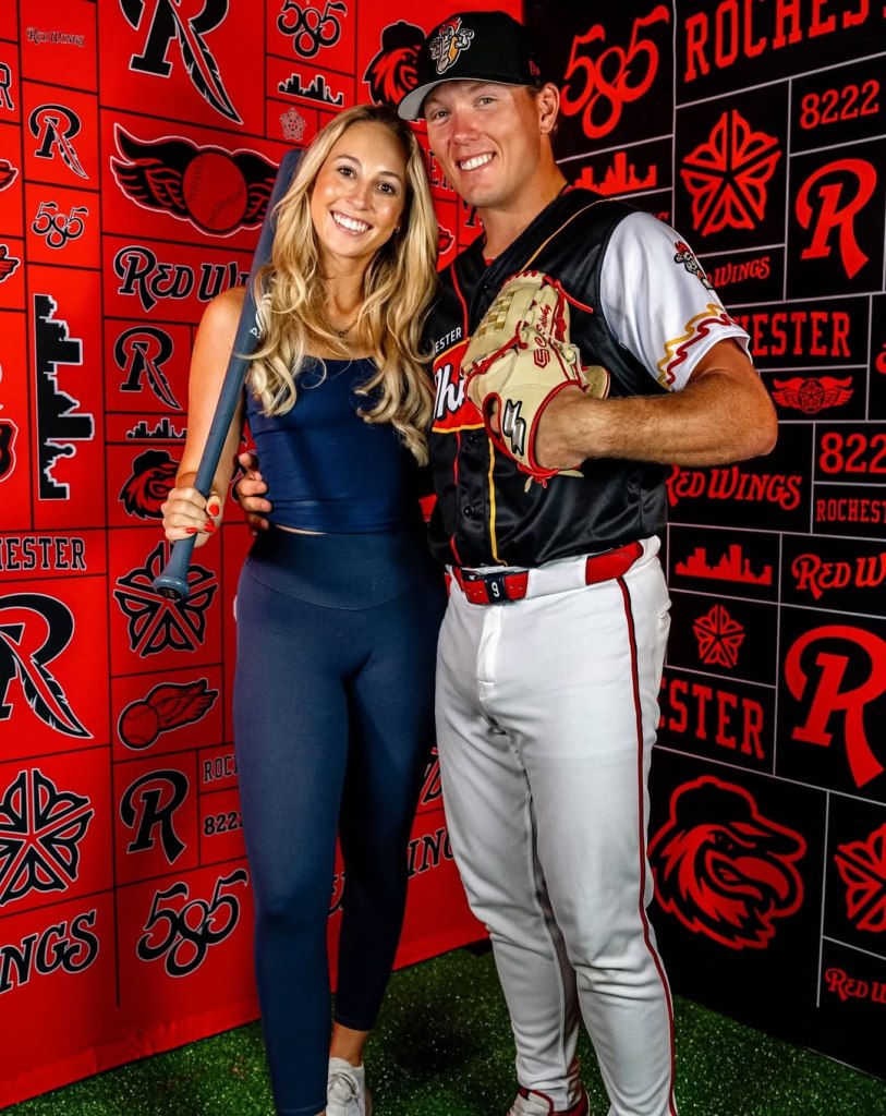 Averee Dovsek and Chase Solesky pose together with baseball equipment against a Rochester Red Wings branded backdrop.