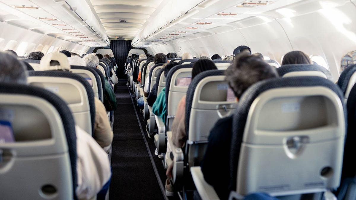Interior of an airplane cabin showing rows of seats along the aisle
