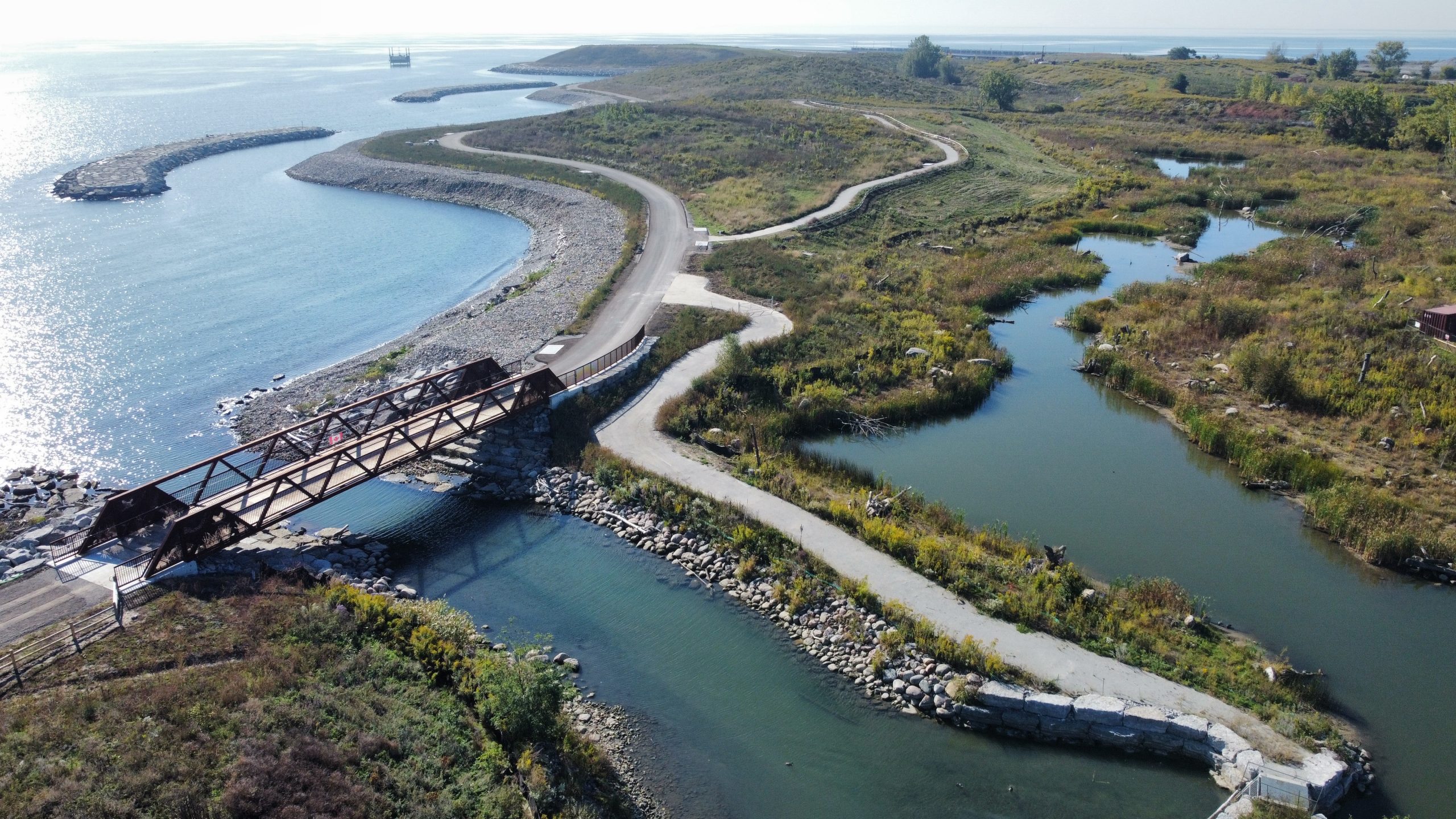 The pedestrian bridge at Jim Tovey Lakeview Conservation Area connects visitors across restored aquatic channels and wetlands along the Lake Ontario shoreline. Designed as part of the conservation area’s accessible trail network, the bridge links visitors to new habitat features, including coastal wetlands, fish habitat areas and the 170-metre wetland boardwalk.