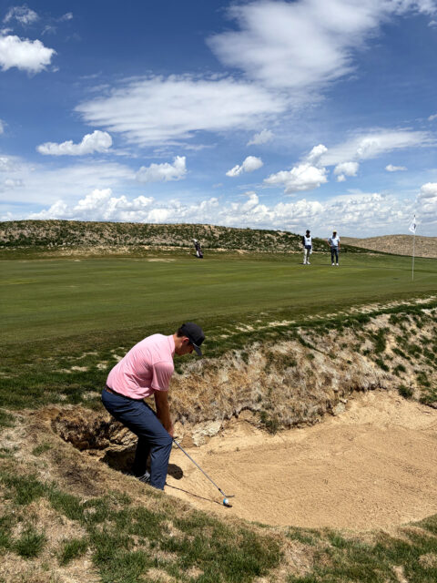 A golfer wearing a pink polo hits out of a bunker at the new Rodeo Dunes golf course in Roggen, Colorado