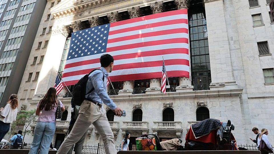 The New York Stock Exchange is seen during morning trading on May 26, 2026. A large American flag hangs from the front of the building and people walk in the street in front of it