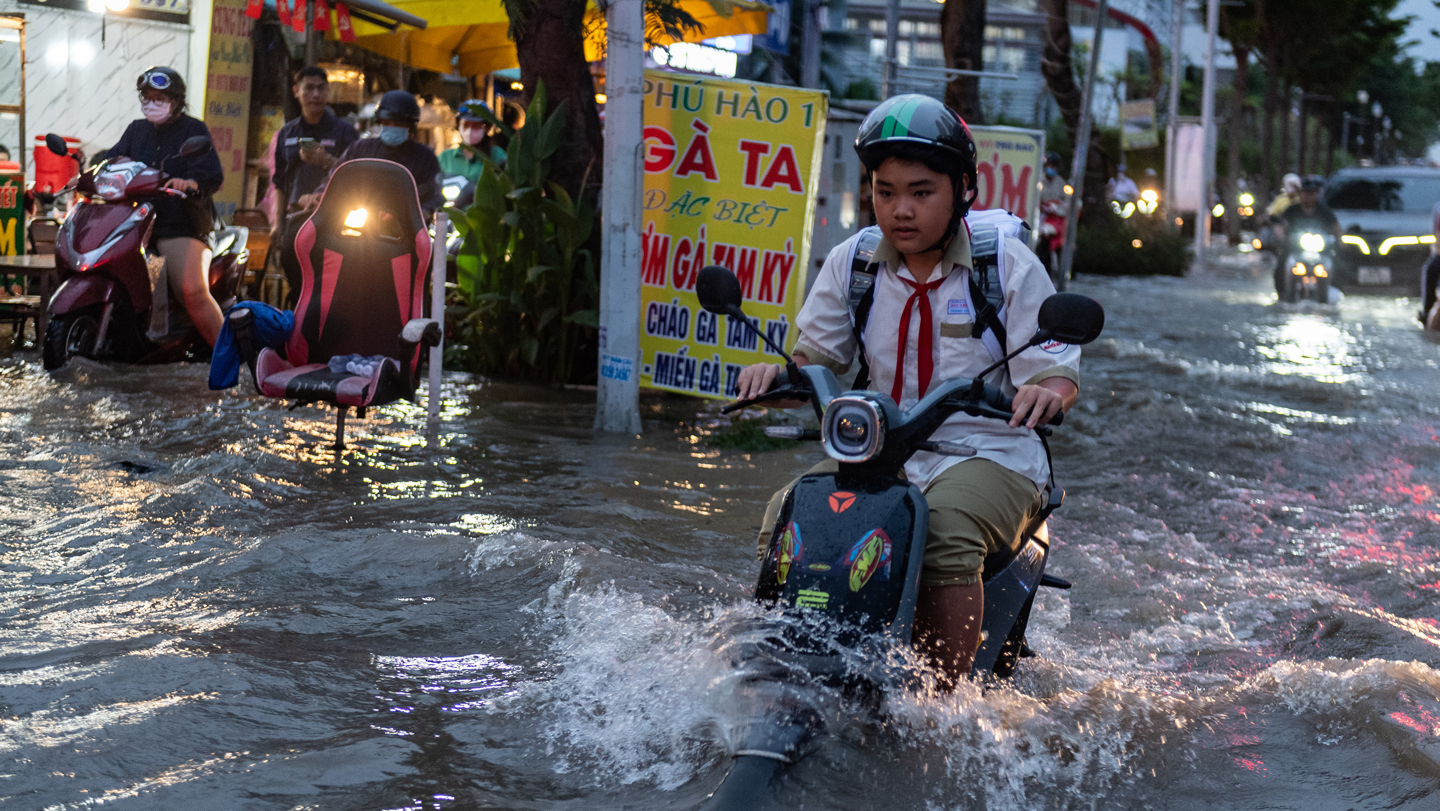 A person drives a motorbike through a flooded street.