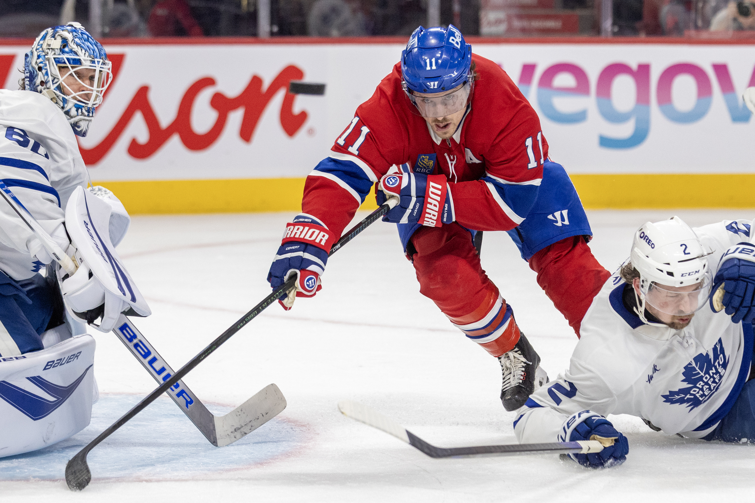 Brendan Gallagher leans forward while skating between a Leafs goalie and skater.