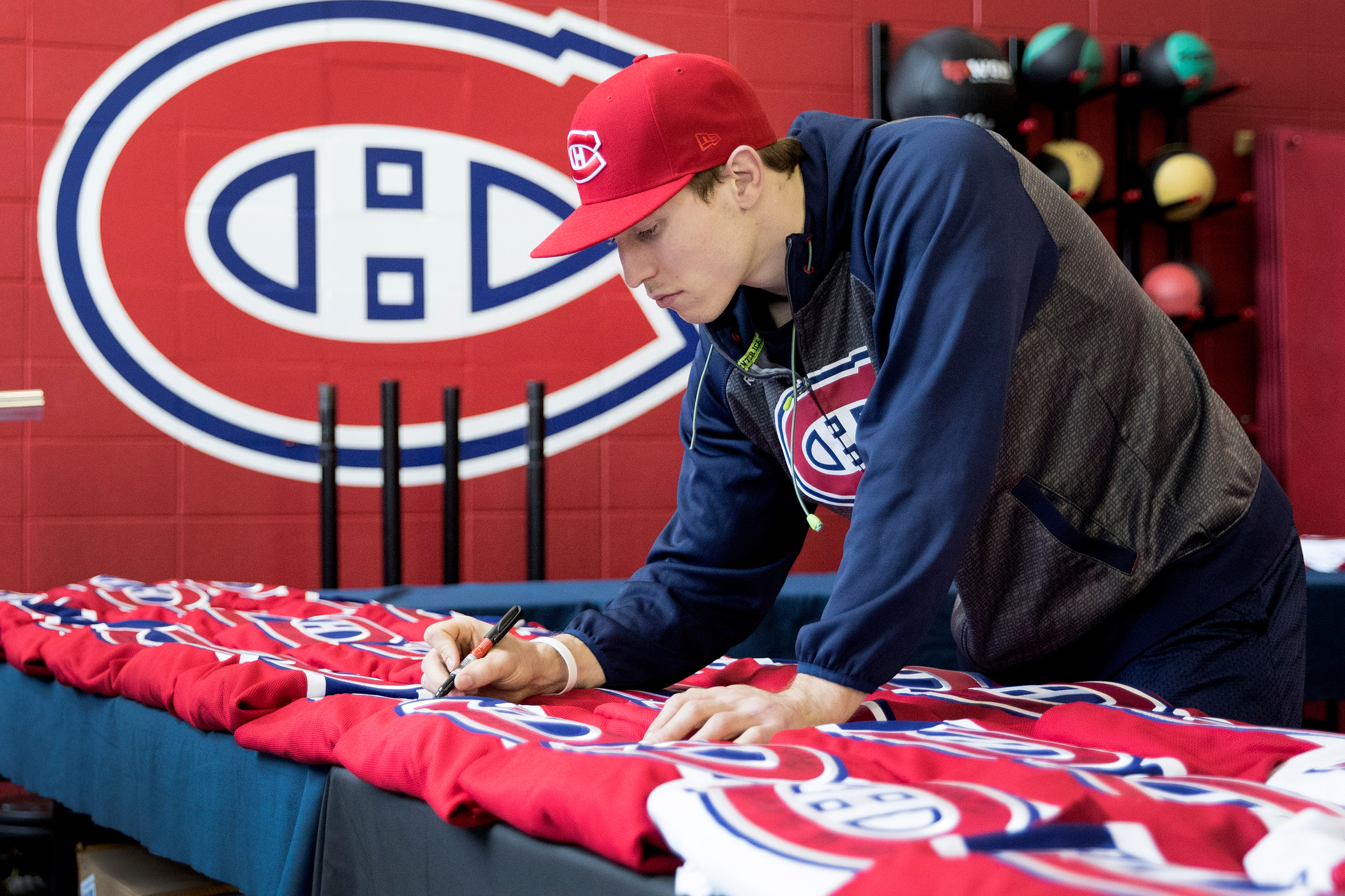 Brendan Gallagher signs Canadiens-branded apparel laid out on a table.