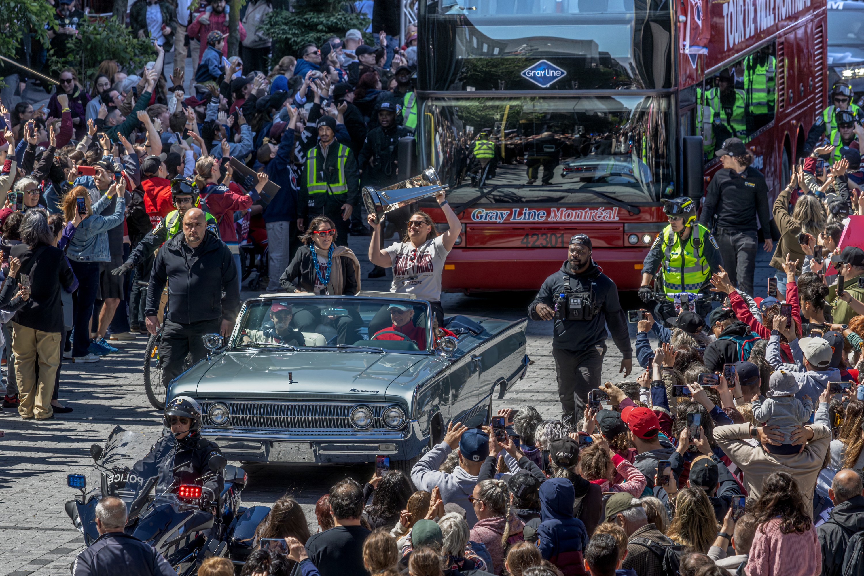 Women's hockey player hoists the championship cup while riding in a convertible. 