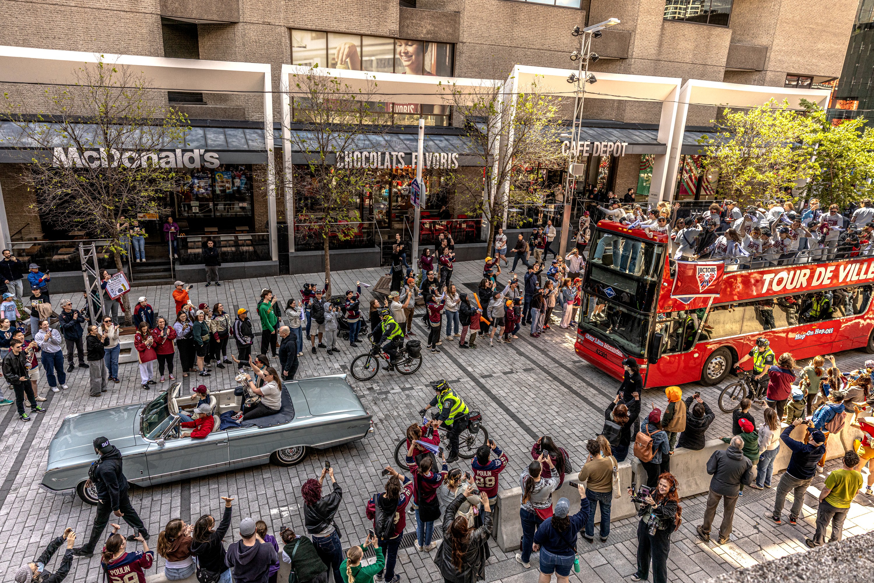 A photo taken from above shows a car and double-decker bus in a parade.