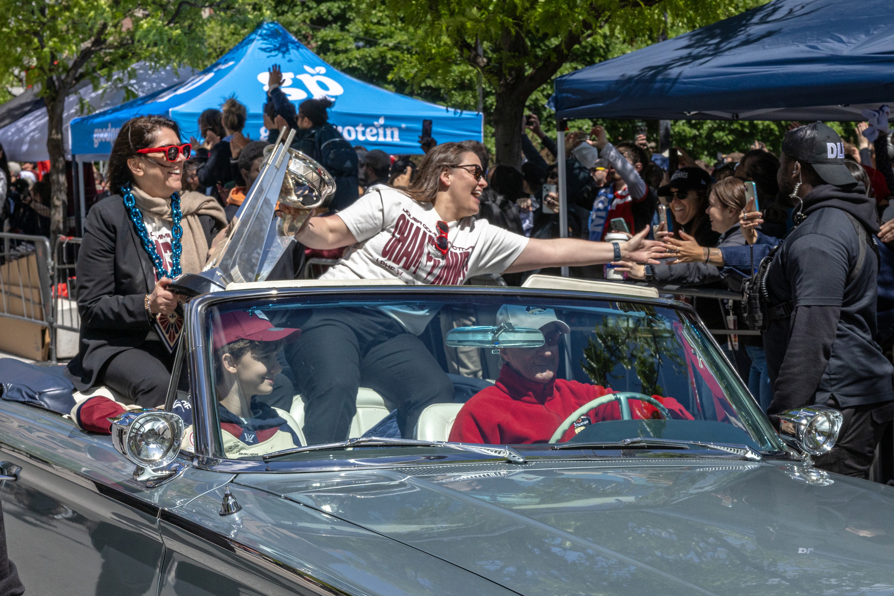 Montreal Victoire team general manager Danièle Sauvageau and head coach Kori Cheverie, left to right, escort the team in a double-decker bus behind in a Mercury convertible with the Walter Cup in hand.  