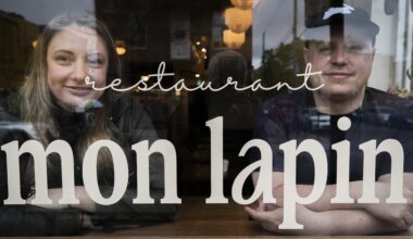 A woman and man sit behind a restaurant window that has the words Restaurant Mon Lapin on it.