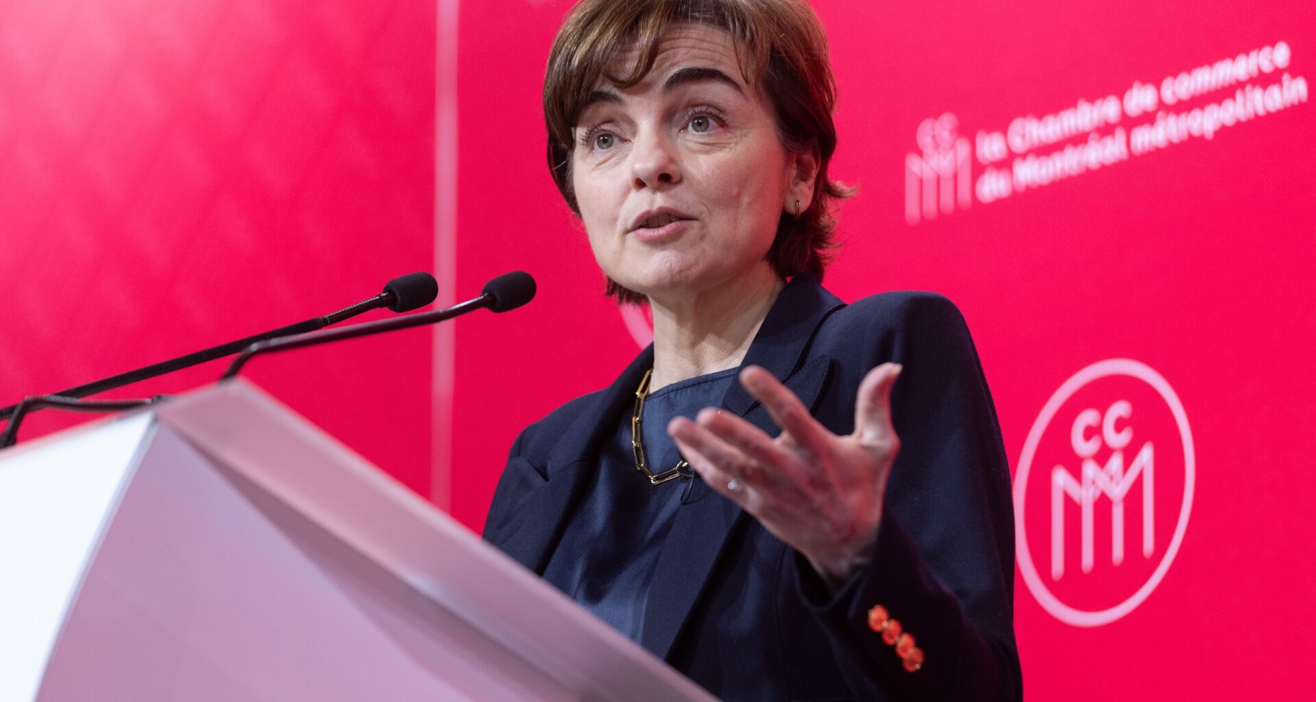 Quebec Premier Christine Fréchette speaks at a podium in front of a red backdrop displaying the logo of the Chamber of Commerce of Metropolitan Montreal.