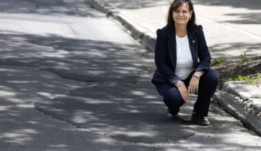 A woman crouches down at the side of a road marked with pothole repairs.