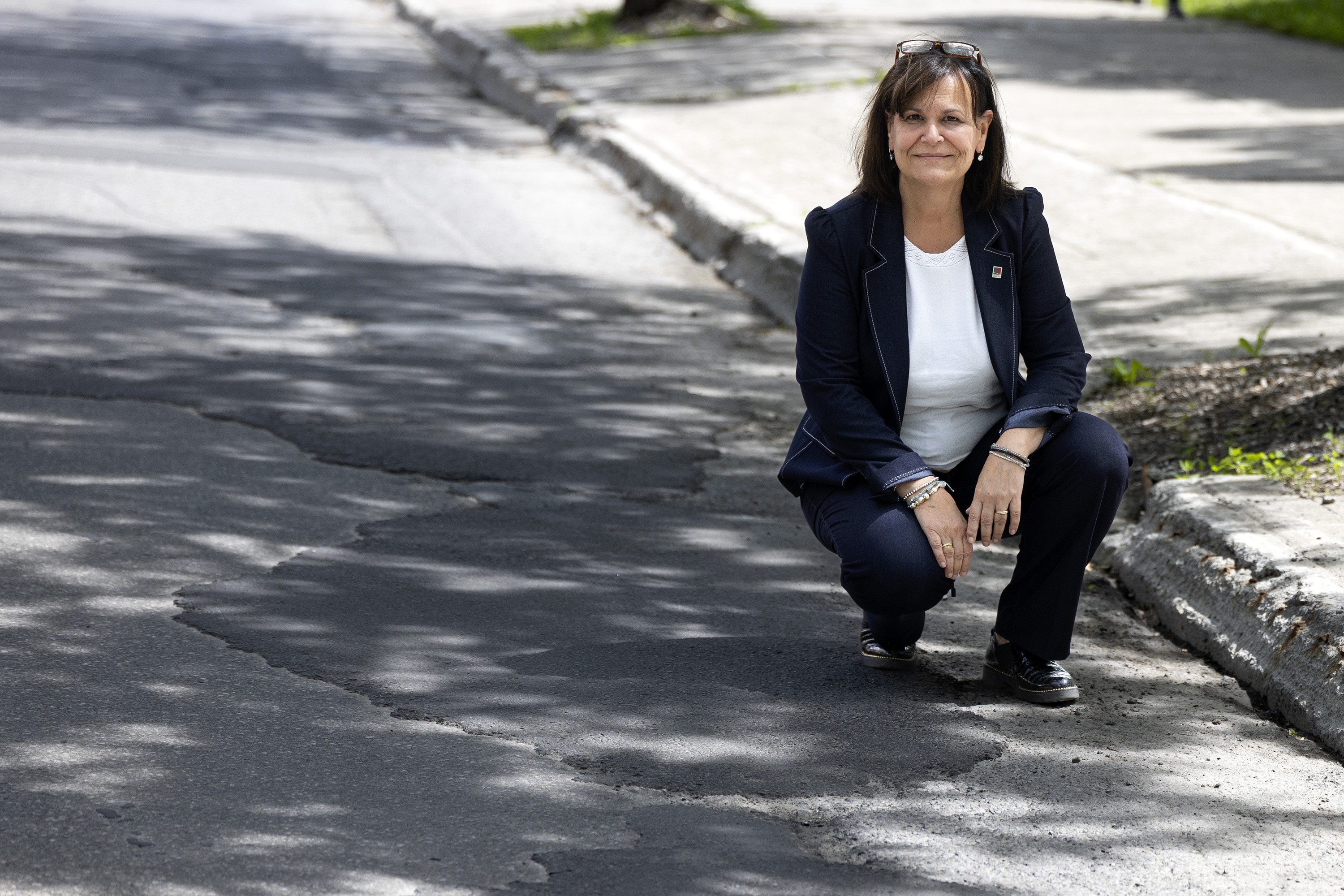 A woman crouches down at the side of a road marked with pothole repairs.