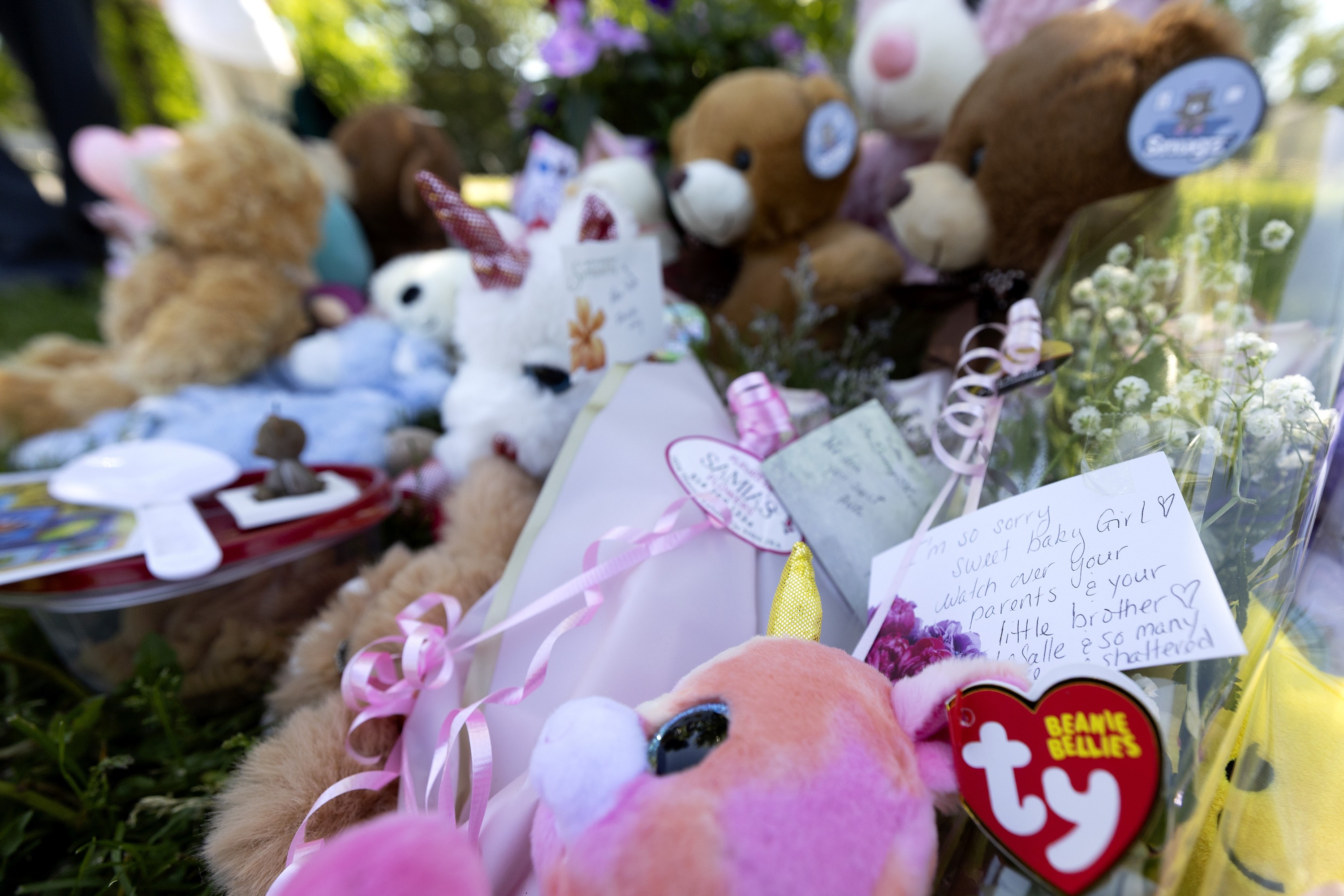 A memorial made up of plush animals, toys and cards is seen among greenery.