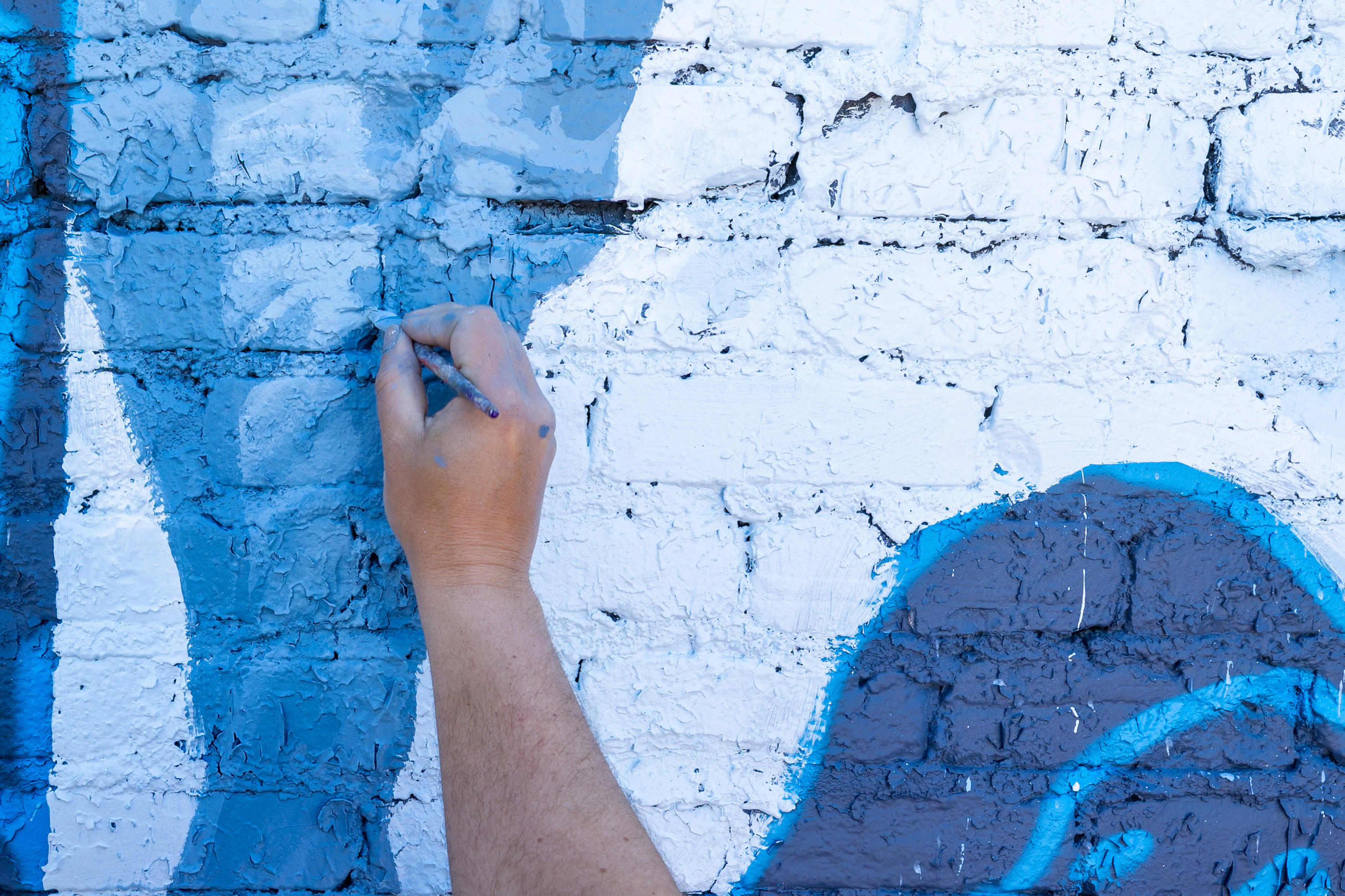 A closeup of a hand painting a mural on the side of a building.