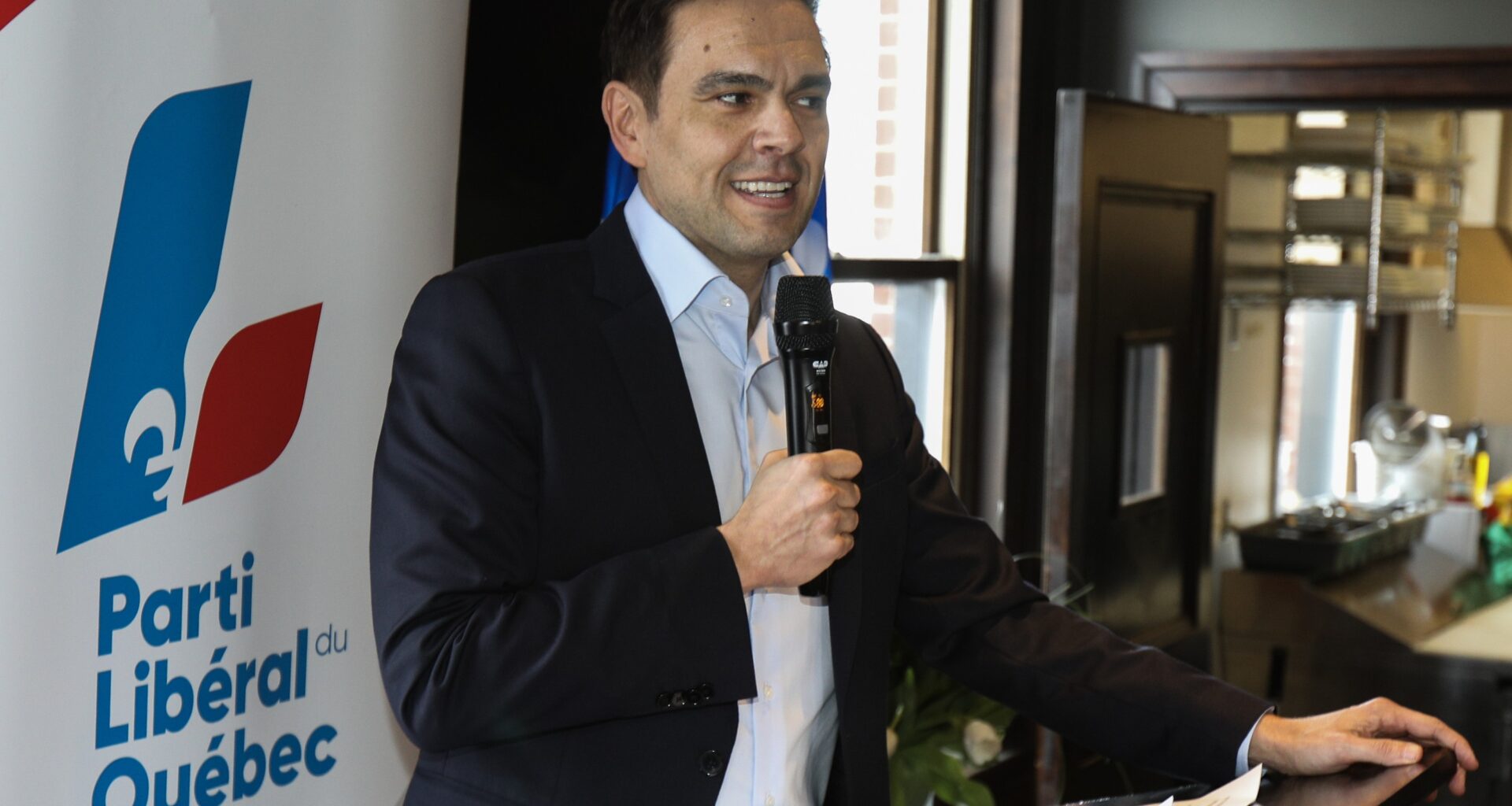 Quebec Liberal Party Leader stands at a podium with a mic in his hand.