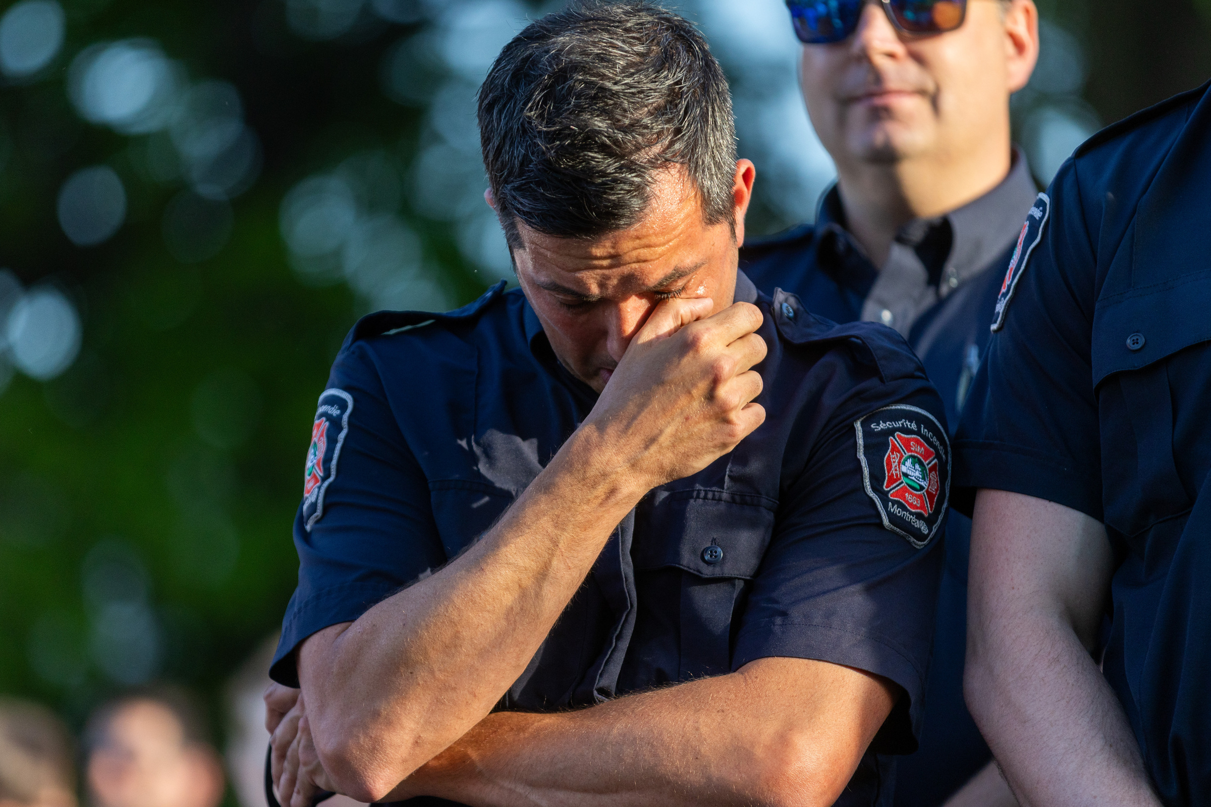 A man in a Montreal firefighter shirt wipes a tear from his eye with his thumb.