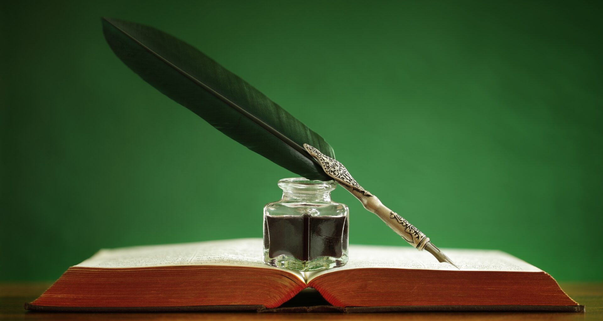 Quill pen and inkwell resting on an old book with green background