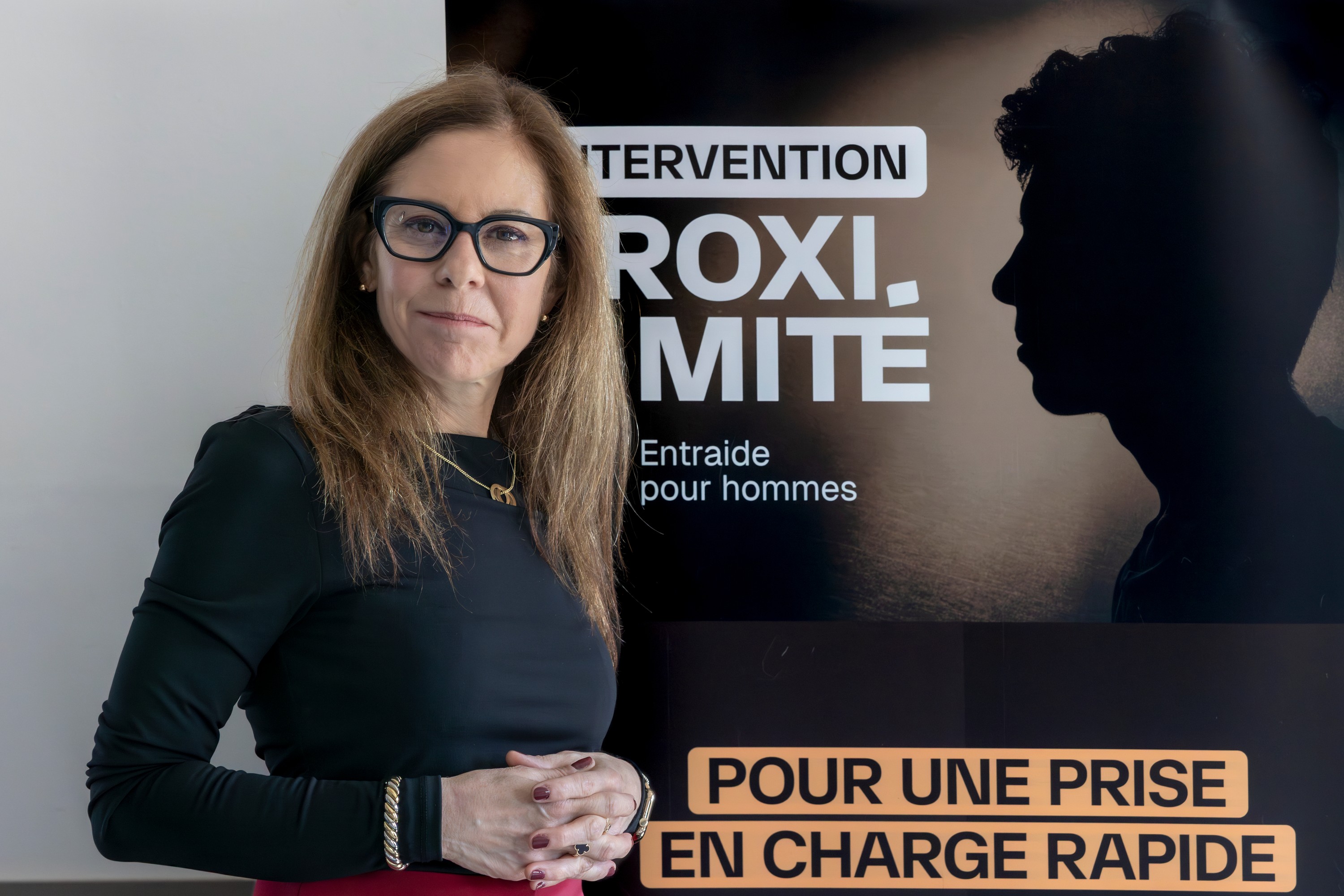 Geneviève Landry, executive director of Entraide pour hommes, stands in front of a sign that shows a man in the shadows as part of an ad about the Projet Proximité.