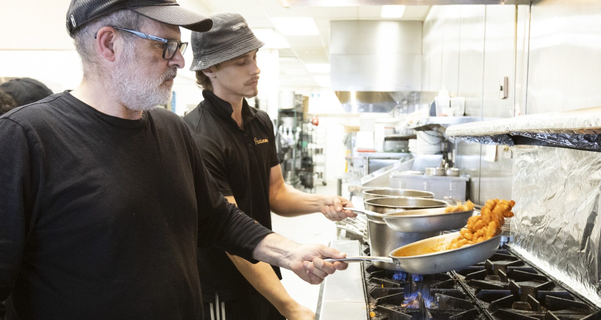 Two cooks prepare pasta over a stove in a restaurant.