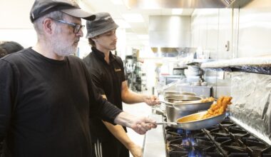 Two cooks prepare pasta over a stove in a restaurant.