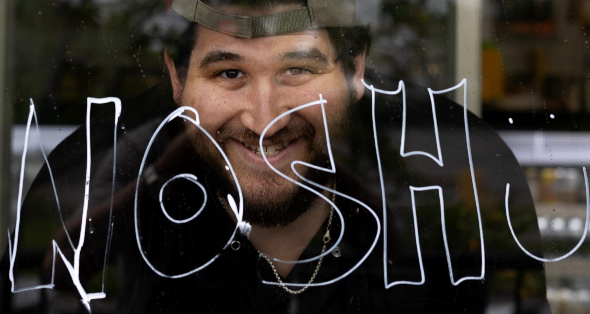 A Montreal restaurant owner in his storefront window that displays the word nosh.