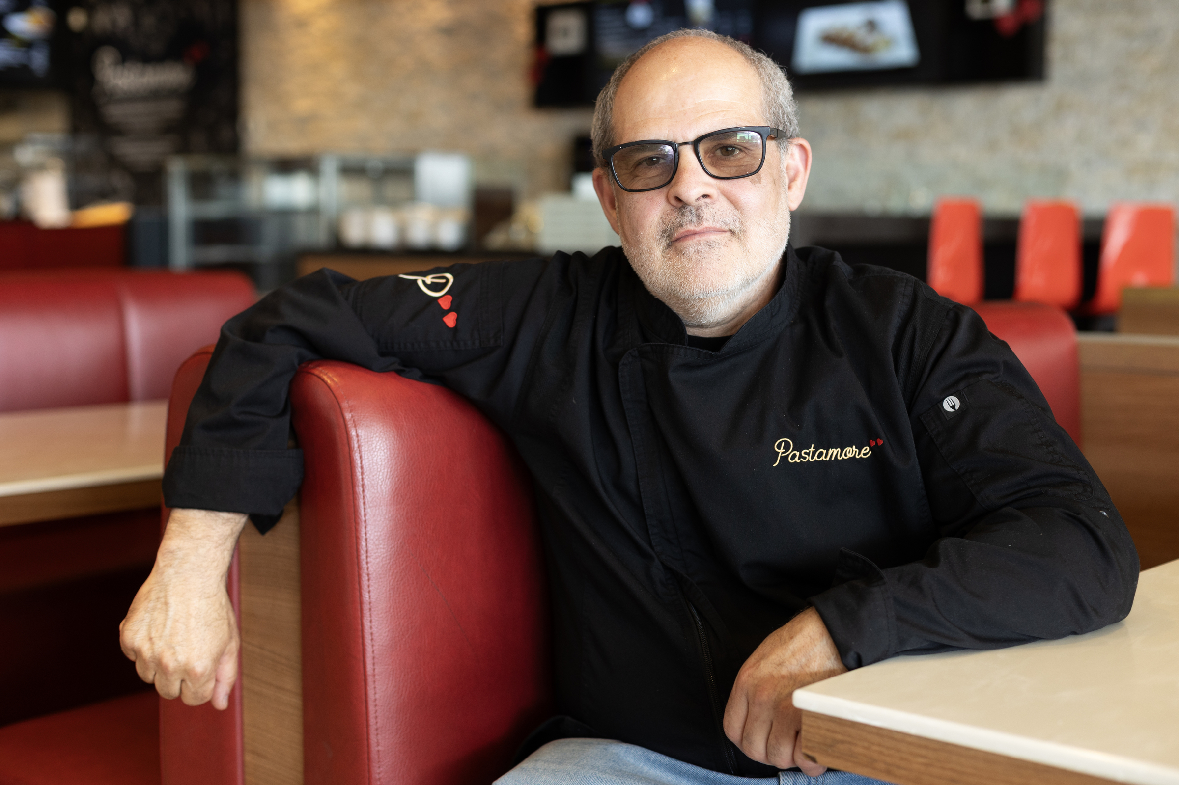 Vincenzo Curro sits at a restaurant table posing for a photo in an empty dining room.