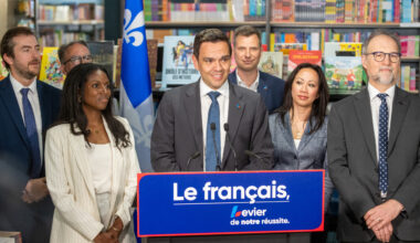 Charles Milliard and other people gather around a podium with shelves of books in the background.