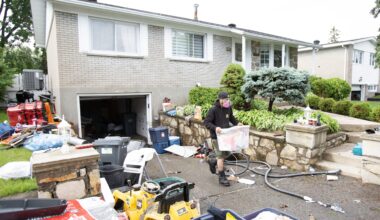 A man wearing a mask carries a container of belongings up a driveway strewn with belongings after flooding.