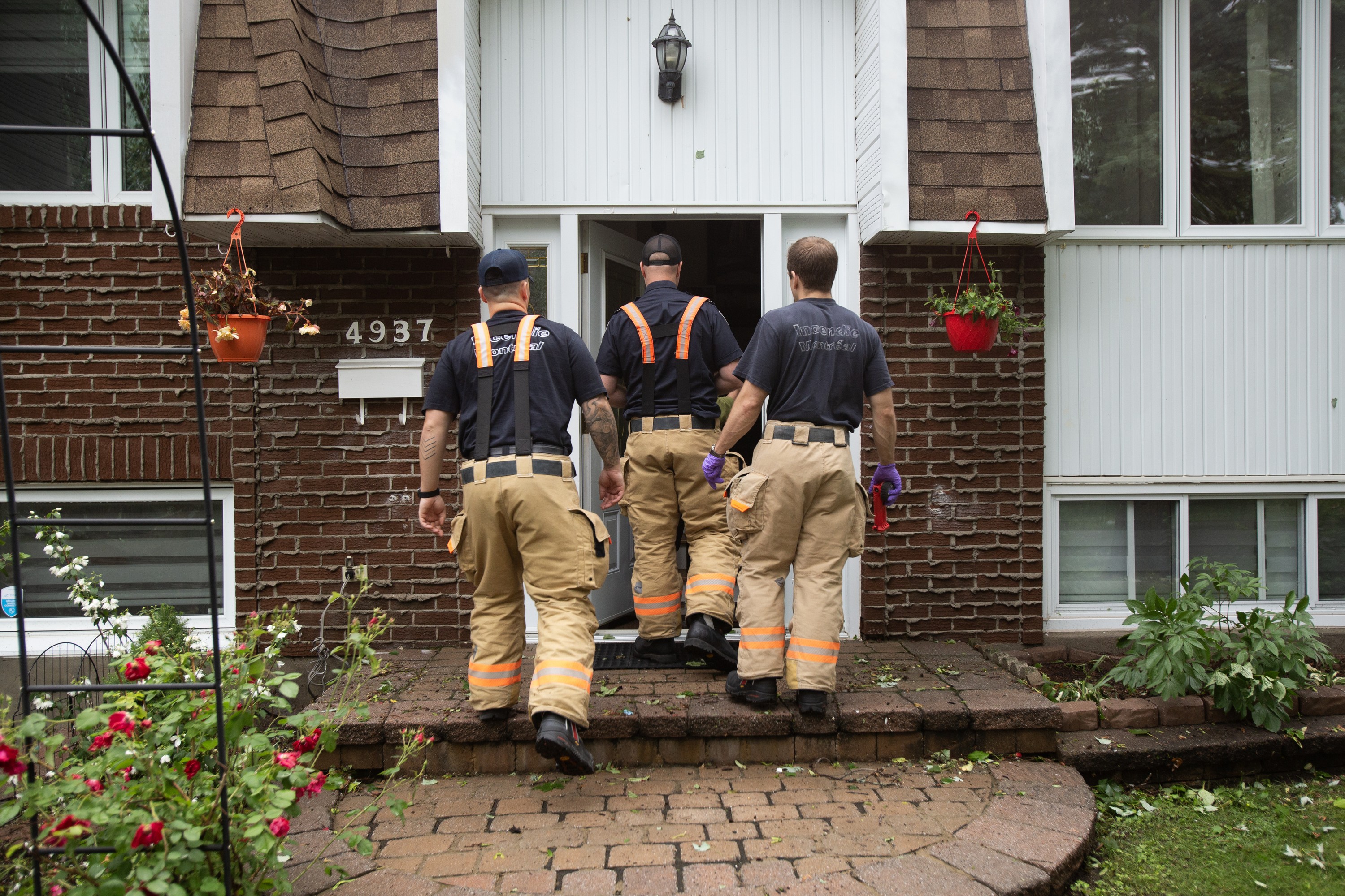 Three firefighters are seen from behind as they enter a home.