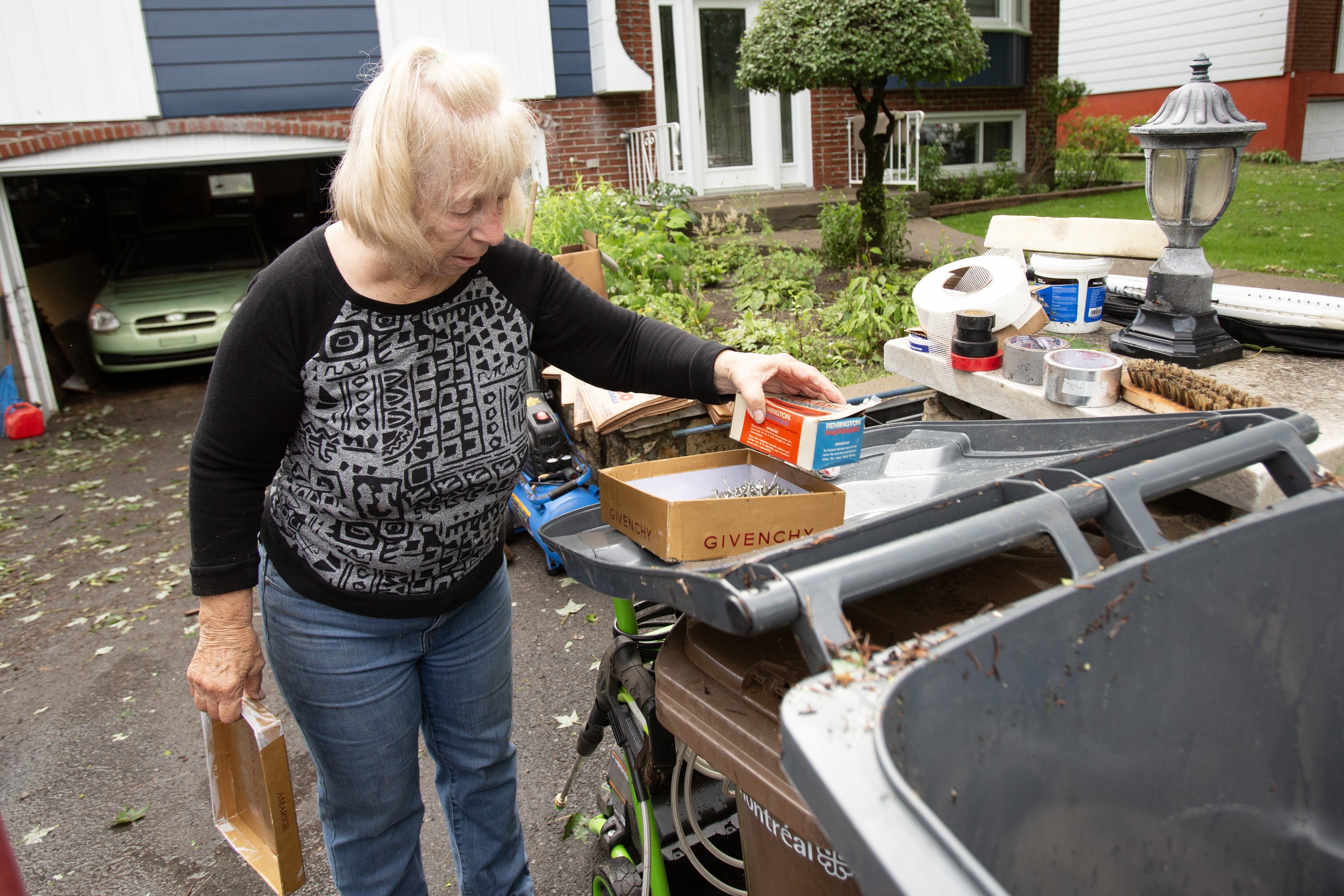 A woman sorts through belongings in a driveway after flooding.