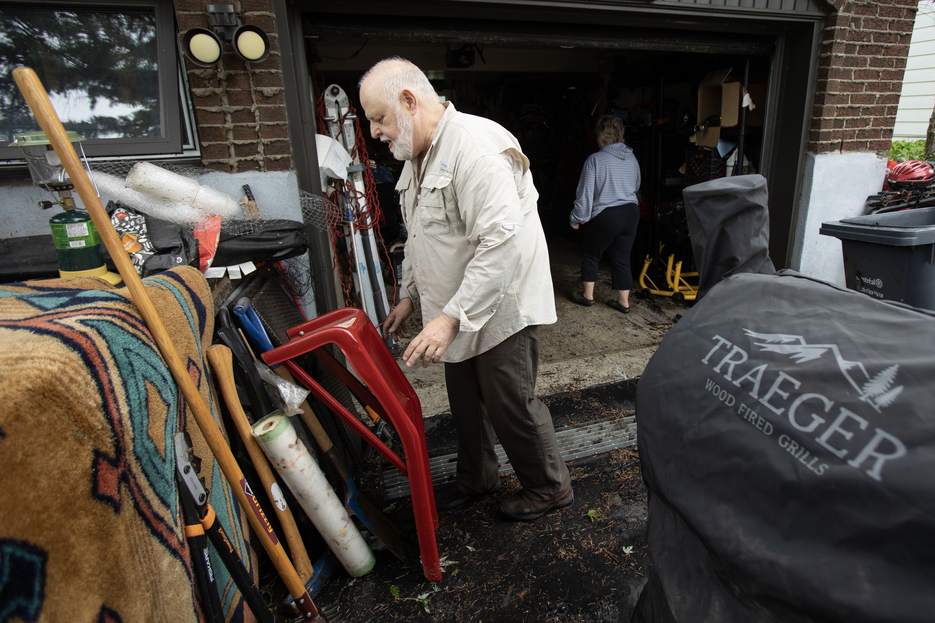A man sorts through flood-damaged possessions outside a garage, as a woman walks inside the garage.