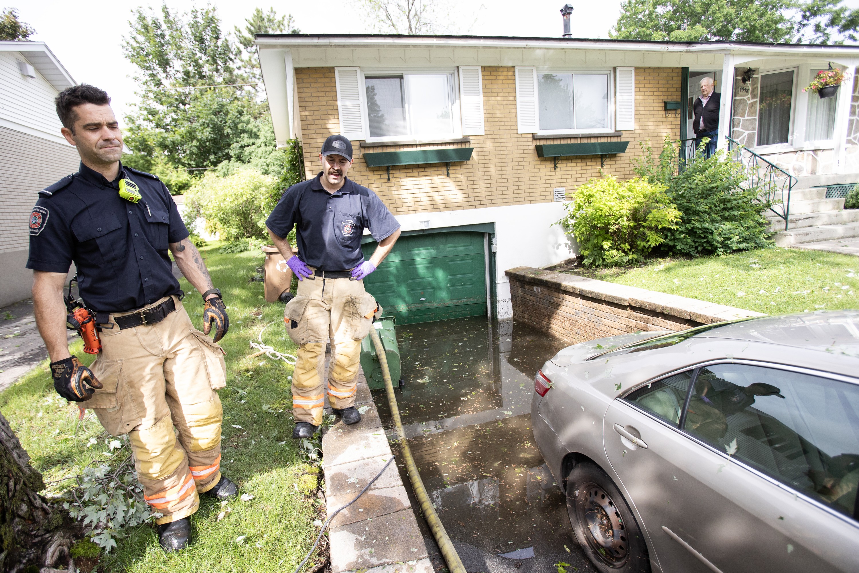 A man watches from his porch as firefighters pump water from his basement.