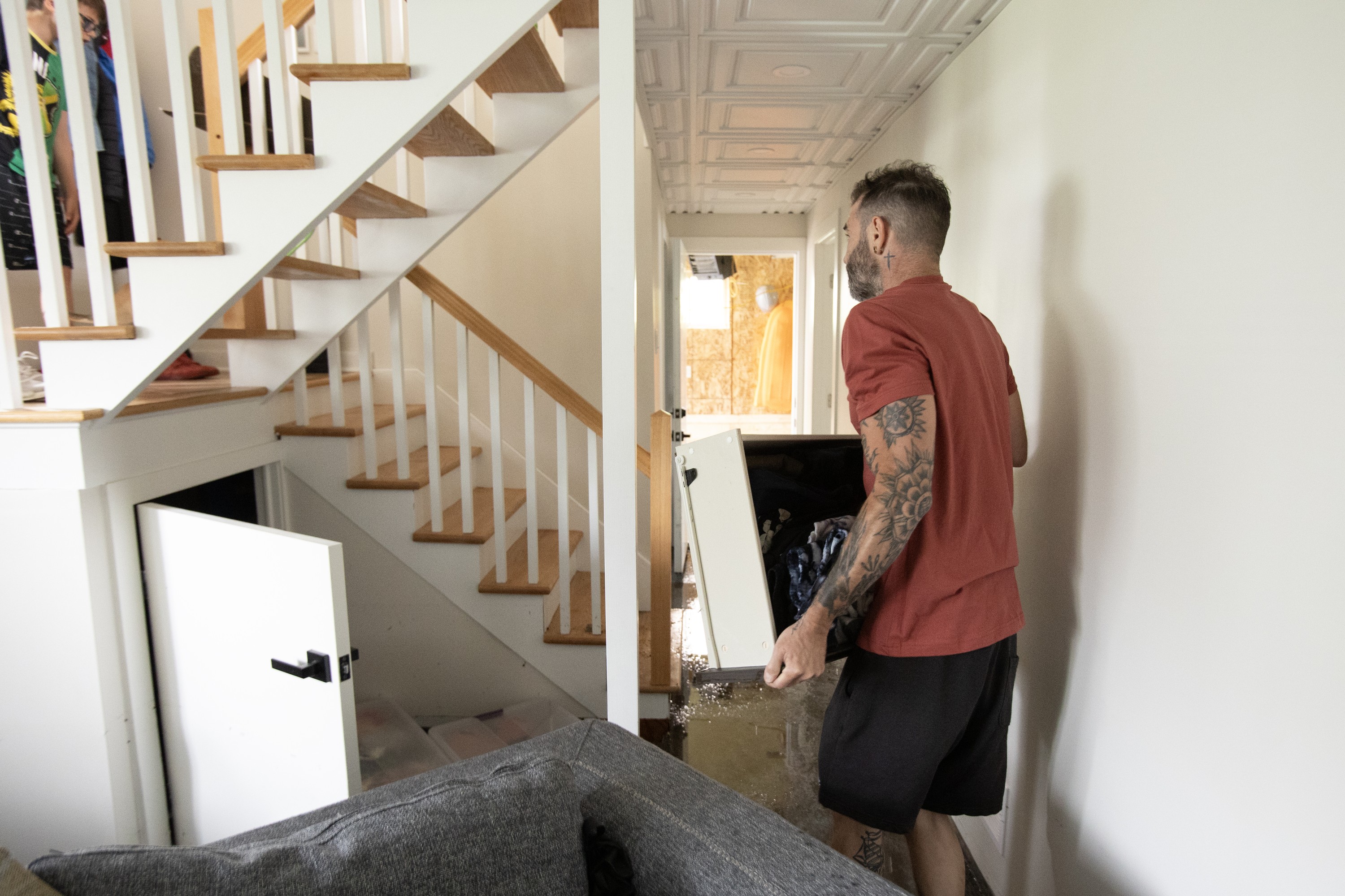A man carries water-soaked possessions in a house after flooding.