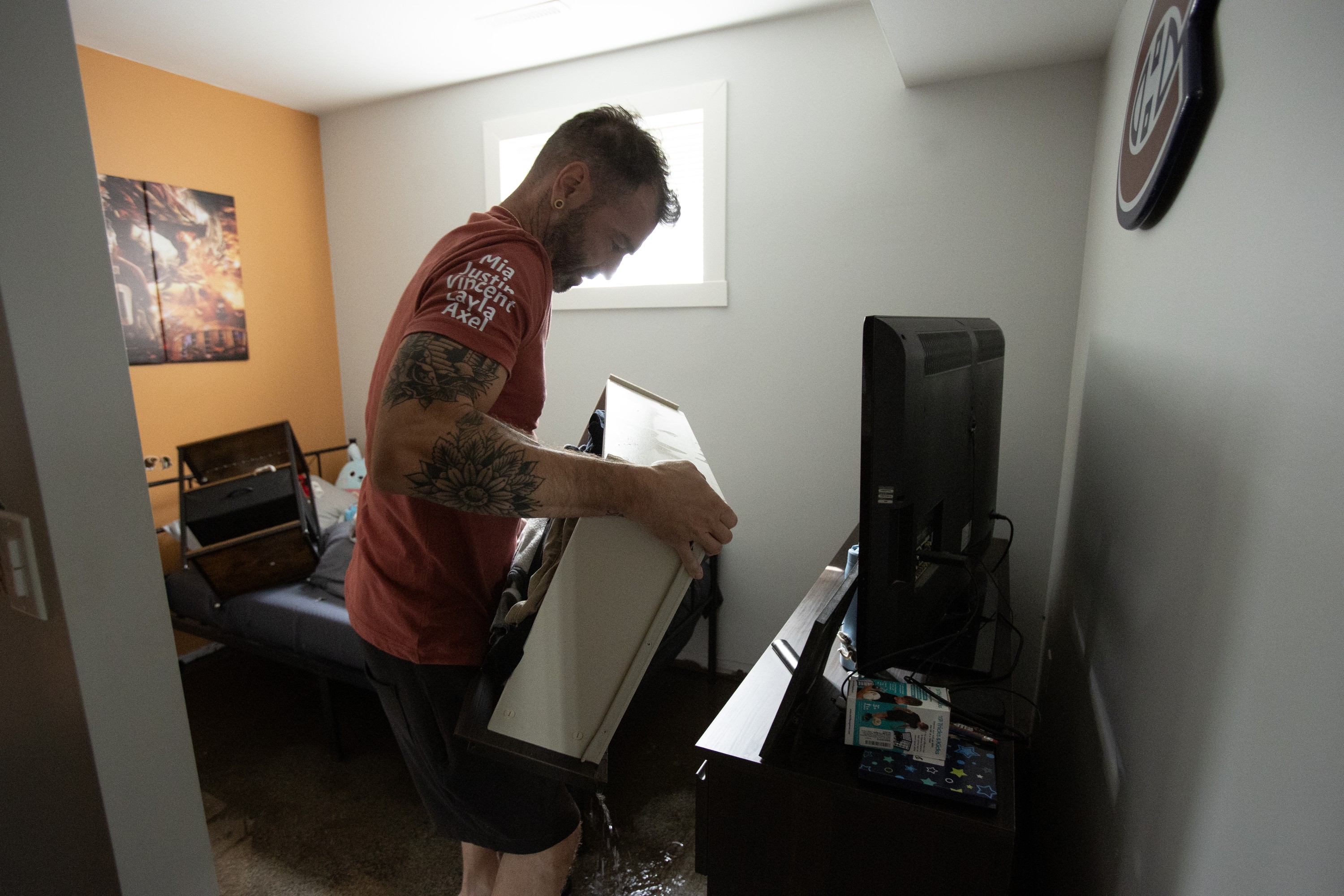 A man carries a water-damaged drawer in a room after flooding.