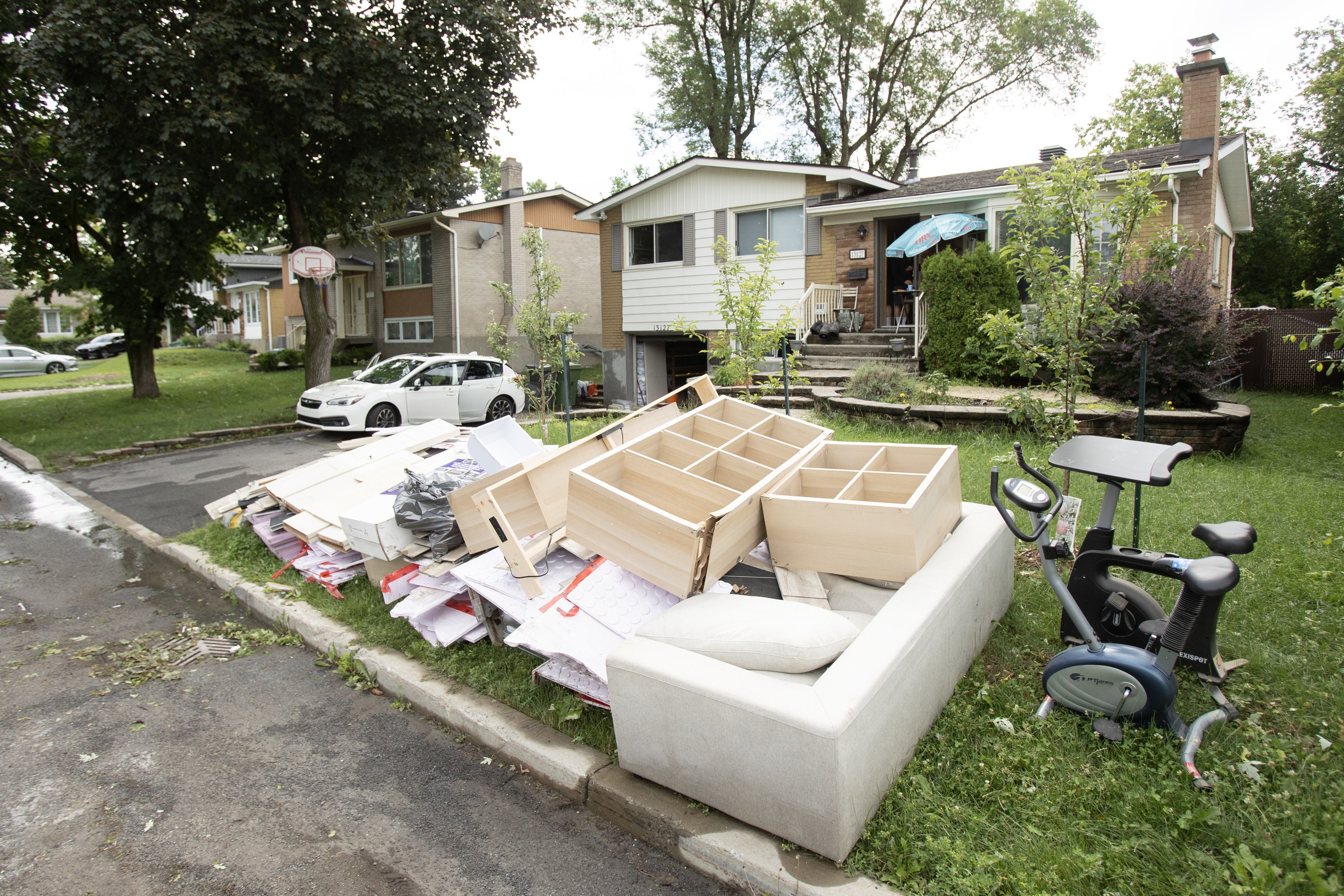 Debris and damaged household items are stacked on the curb in front of a house, including a couch and cupboards.