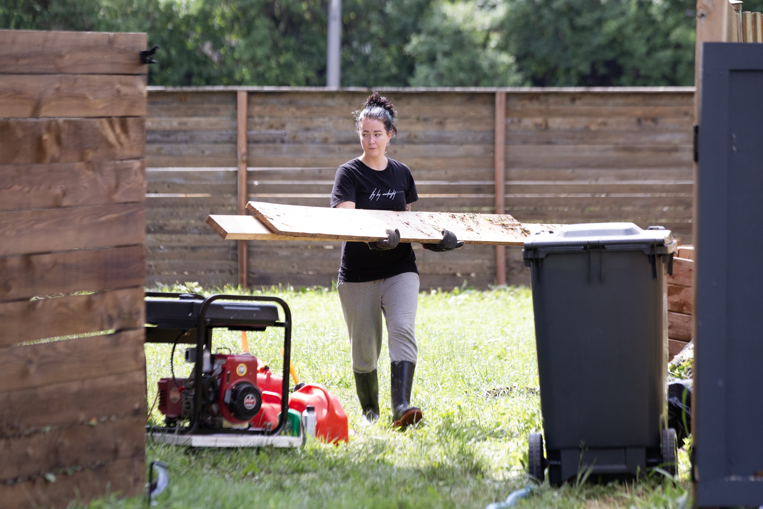 A woman carries strips of lumber through the yard of a home.
