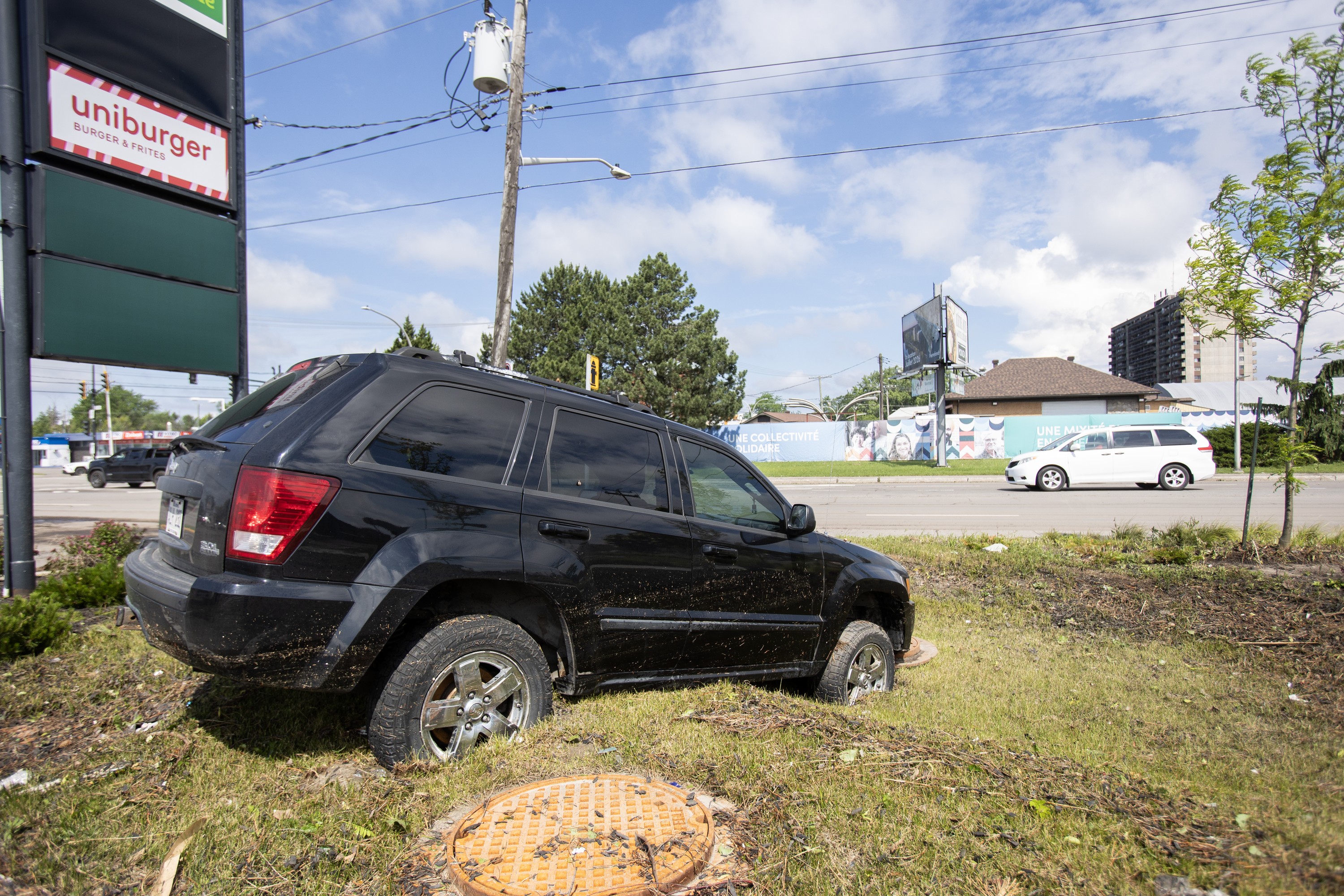 A car sits in a ditch in front of a sign that says Uniburger, with a road in the background.