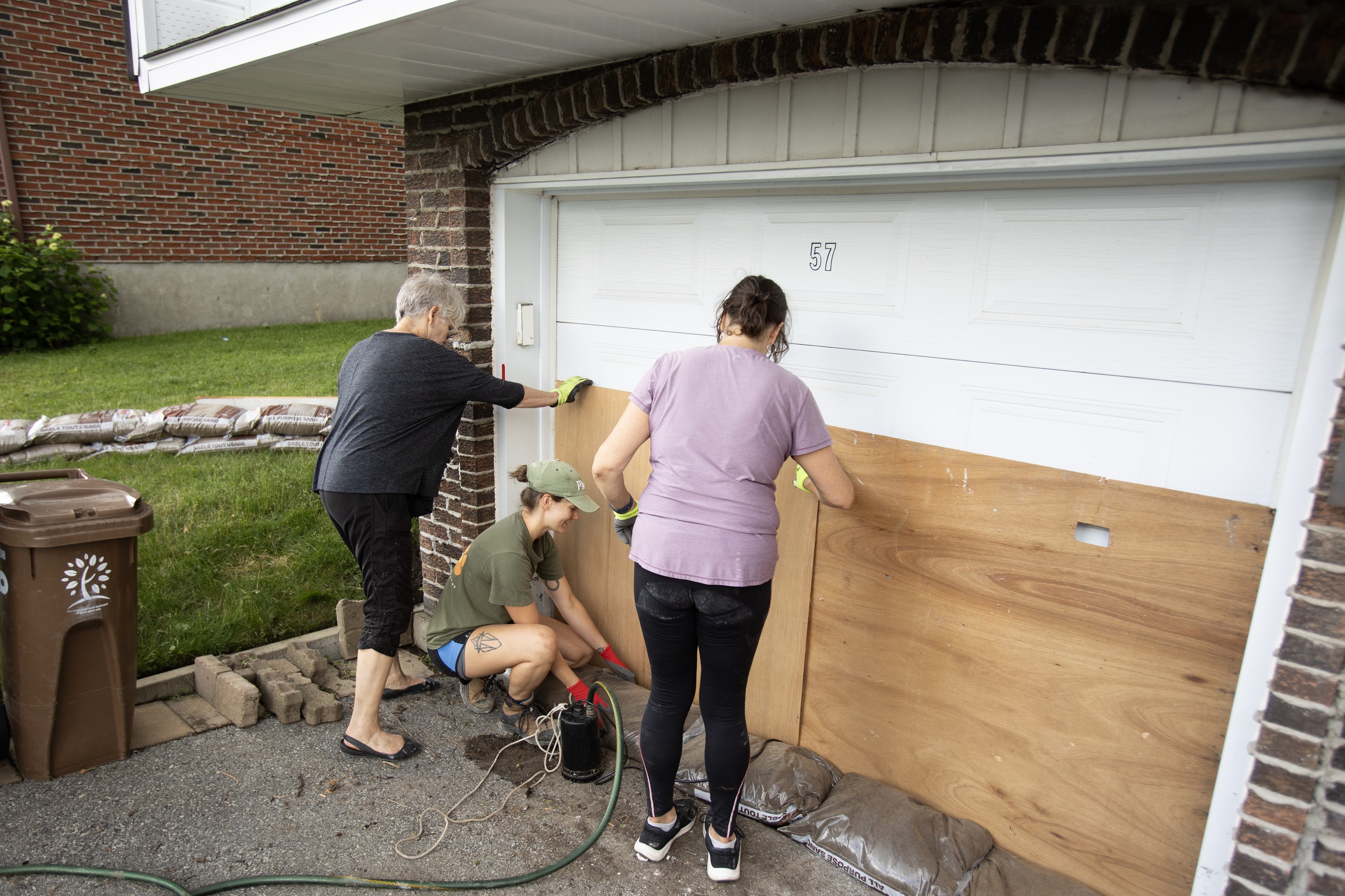 Three women use wood panelling to block a home's damaged garage door.