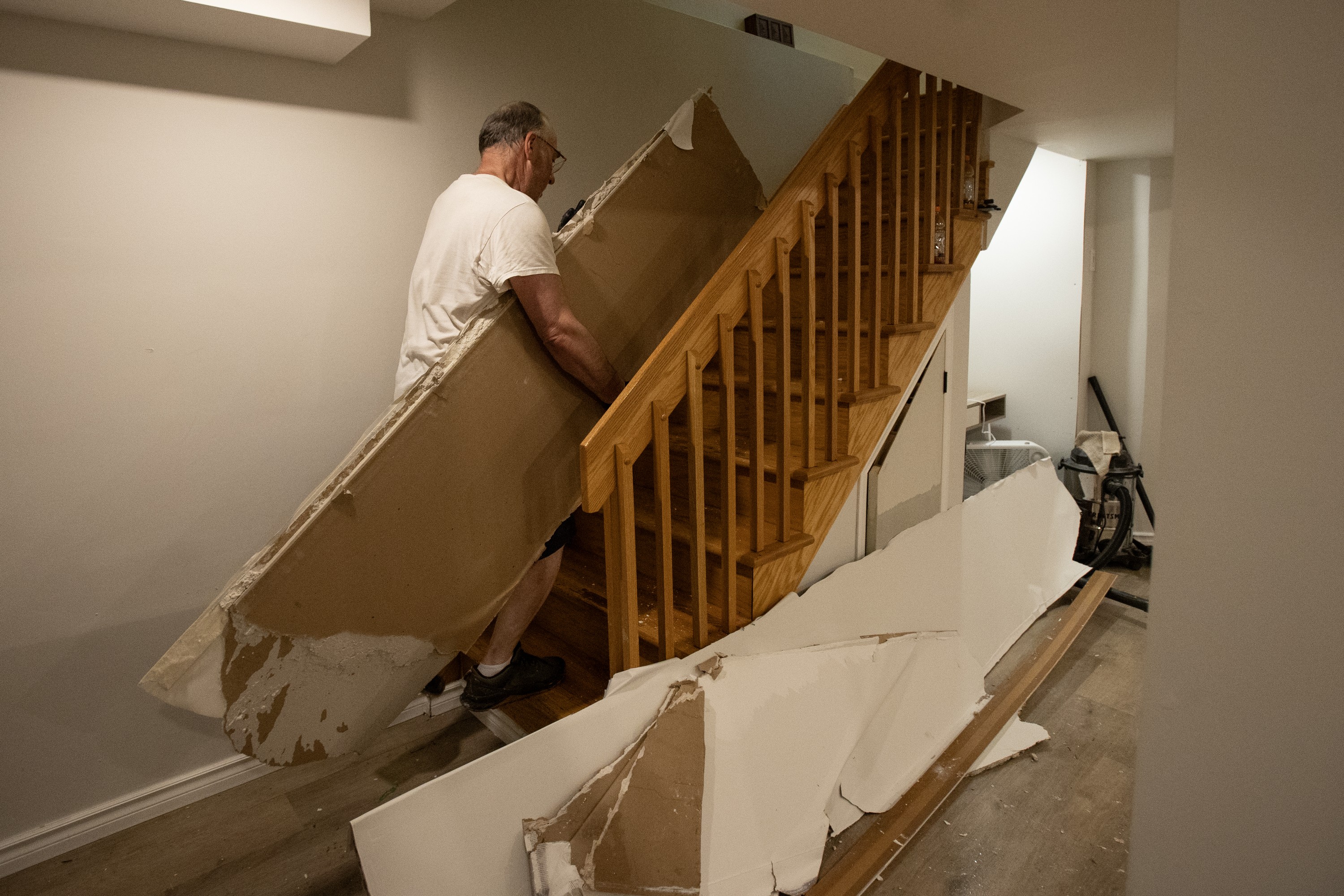 A man carries long pieces of damaged household material up a staircase, as more damaged pieces rest against the bottom of the stairs.